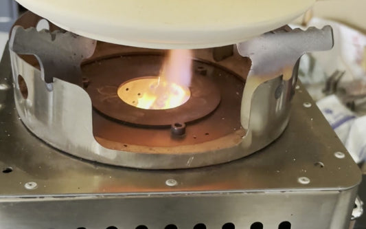 Hillrein Zhengtu fuel efficient wood stove close-up showing visible flame beneath the pale base of a kettle held above the circular burn opening